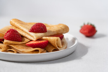 Thin crepes with strawberries in plate on light background. Morning breakfast concept