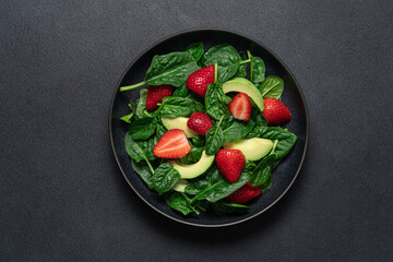 Strawberry salad with avocado and spinach in black plate on dark background. Seasonal dietary healthy salad