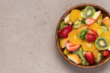 Fruit salad in wooden bowl on beige background. Kiwi, orange, strawberry, apple, pear top view