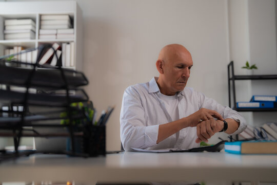 Focused mature businessman sitting at desk looking at his smartwatch, managing his schedule and organizing his time in a bright modern office