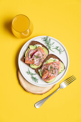 Smoked salmon avocado sandwich on yellow background. Black whole grain bread, avocado, salted salmon and dill for healthy breakfast