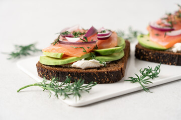 Smoked salmon avocado sandwich on light background. Black whole grain bread, avocado, salted salmon and dill for healthy breakfast