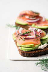 Smoked salmon avocado sandwich on light background. Black whole grain bread, avocado, salted salmon and dill for healthy breakfast