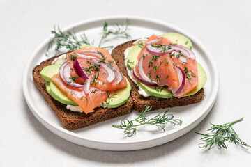Smoked salmon avocado sandwich on light background. Black whole grain bread, avocado, salted salmon and dill for healthy breakfast