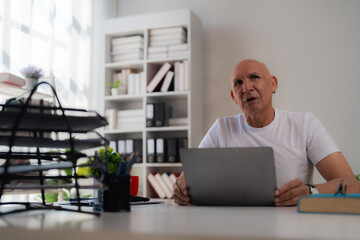 Surprised mature businessman having a video conference on laptop in office, looking up with astonishment, sitting at desk, working from home