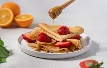 Thin crepes with strawberries and honey in plate on light background. Morning breakfast concept