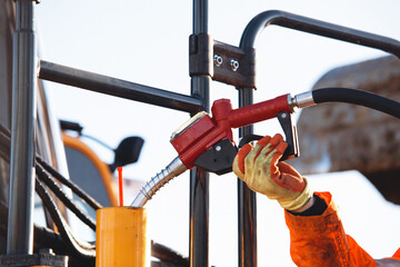 Close-up of worker wearing gloves refuels heavy machinery using red fuel pump nozzle