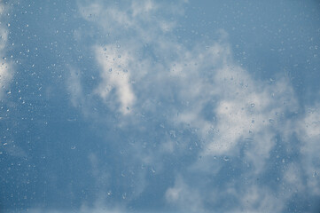 Rain drops sliding on glass with cloudy sky in background