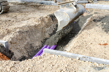 Construction site showing excavation for utility installation with equipment pouring concrete over...