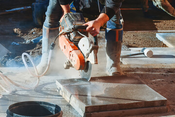 Construction worker cutting concrete paving tiles with petrol concrete cutter saw and water dust...