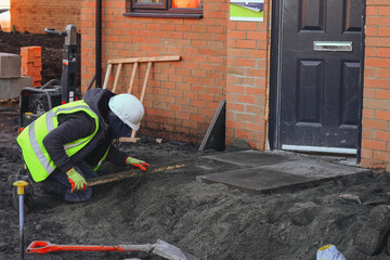 Obraz premium Construction worker lays concrete paving slab for front door access landing area