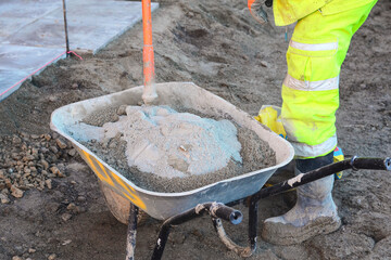Builder mixing sand and cement mix in wheelbarrow at construction site