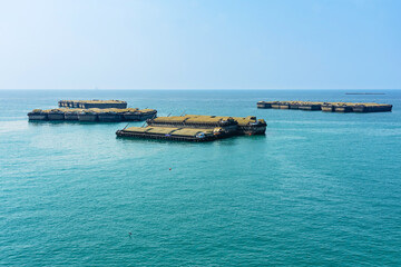 Large cargo barge in sea. Large tugboat anchored to avoid monsoon storm at back of island. Tugboat cargo carry products. Importance of river transport in transporting goods and developing economy.