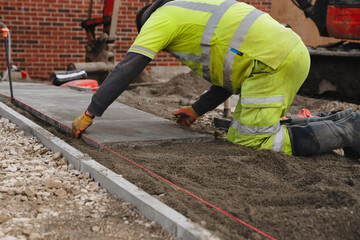Construction worker laying concrete paving slabs at building site