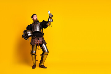 Naklejka premium Young man in medieval knight armor using a smartphone against yellow background