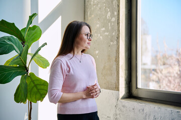 Middle aged calm beautiful woman looking out window