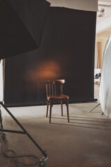 Empty wooden chair illuminated softly in a photography studio, inviting creativity and contemplation in a minimalist setting during daylight hours.