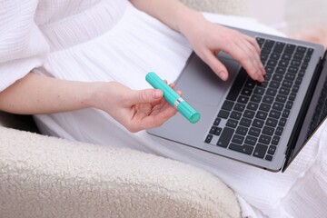 Beauty blogger with mascara using laptop in armchair indoors, closeup
