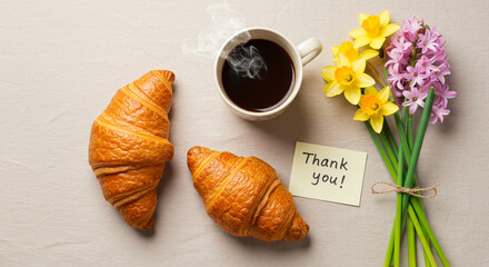 Breakfast with flowers and gratitude, featuring croissants, coffee, and a 'thank you' note.