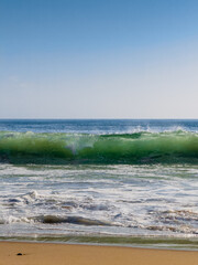 Low angle view of a powerful breaking wave at sandy beach on a sunny day 