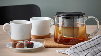 Closeup of teapot and white mugs on cork coasters.