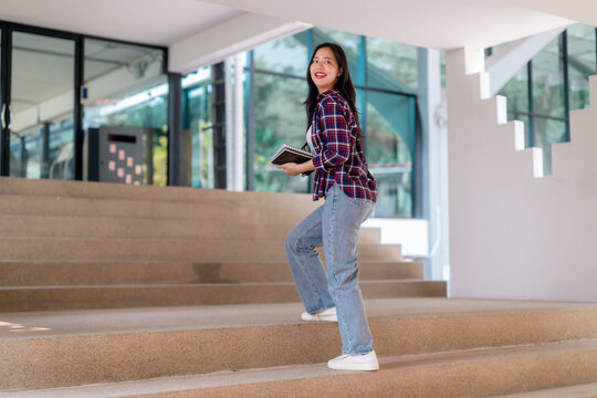 Female student climbing campus steps, gripping textbooks, beaming with academic enthusiasm and collegiate energy