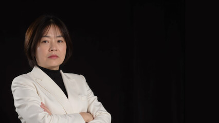 Closeup of stern looking asian business woman in a white suit on black background.
