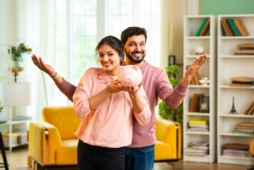 Happy Indian couple holds and shakes piggy bank together, promoting smart saving habits
