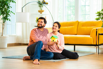 Smiling Asian couple holding colorful paper house model while planning new home in living room