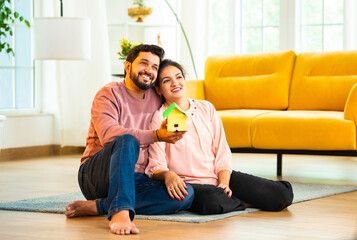 Smiling Asian couple holding colorful paper house model while planning new home in living room