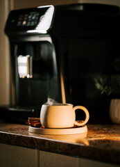 Steaming cup of coffee placed on a wooden coaster near a coffee maker in a cozy kitchen setting