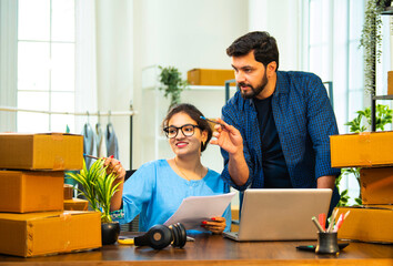 Indian Asian entrepreneurs verifying cardboard box dispatch list on paper at store office desk