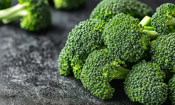 Fresh, vibrant green broccoli florets rest on a dark, textured, and appetizing surface.