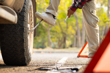 A man sets up a reflective triangle to warn other drivers to be careful of cars parked on side of the road. A man sets up an orange reflective triangle on the side of the road to change a flat tire.