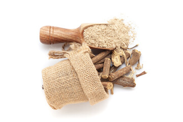 A scoop of organic Liquorice or Mulethi (Glycyrrhiza glabra) powder, along with liquorice roots spilled out from a jute bag. Isolated on a white background.