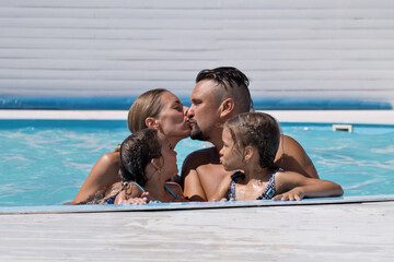 The family rejoices and swims in the blue pool at the hotel. Mom, dad, and daughter are on vacation at sea.