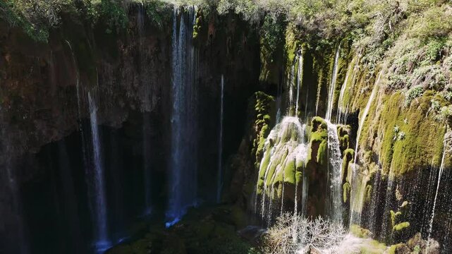 Vivid sunlight streaming over yerkopru waterfall, cascading through moss-covered rocky canyon with shadowy depths plunging into untouched wilderness landscape