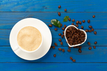 Cup of coffee with coffee beans and leaves on wooden background,top view