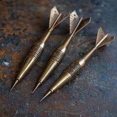 Three Brass-Toned Darts with Grooved Midsection and Stabilizing Fletching on a Textured Surface