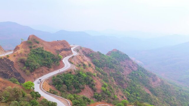 Aerial view bendy trail cuts craggy hill under hazy sky