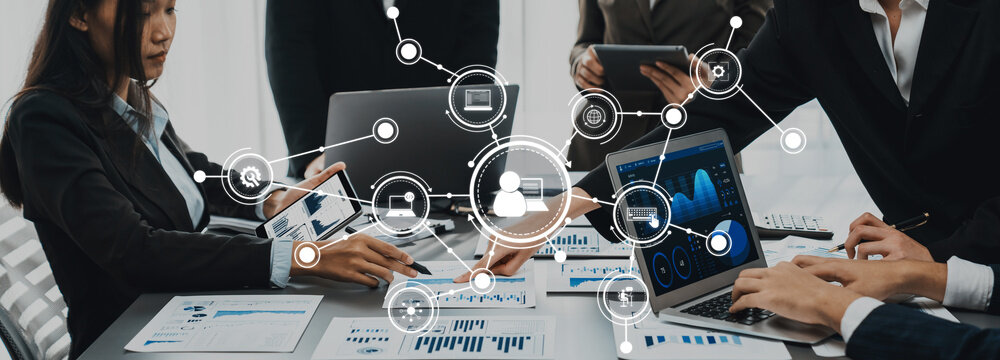 A group of professionals engages in a business meeting, utilizing digital devices to analyze data and collaborate effectively. The scene showcases modern office dynamics. Amity