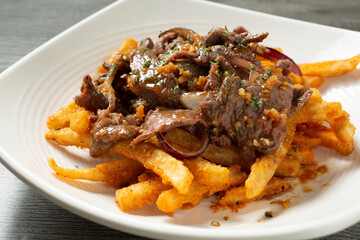 A view of a french fries, topped with stir fry beef.