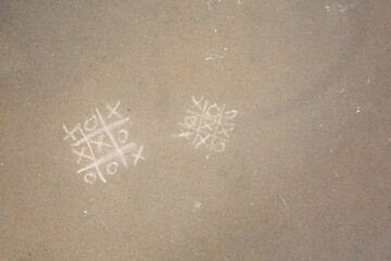 A top down view of a tic tac toe game drawn in chalk, seen on a sidewalk surface.
