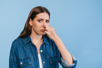Beautiful young woman girl in casual clothes and long brown hair smelling stinky, closing her nose...