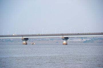 Distant bridge spans a wide river with cars driving across against a hazy sky.