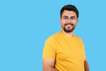 Obraz premium Indoor portrait of young european caucasian man isolated on blue background, standing in yellow t-shirt , smiling and looking straight at camera.