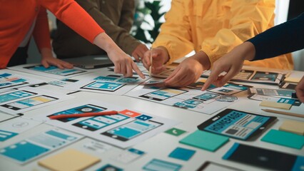 Obraz premium A diverse group of individuals collaborates on user interface mockups at a table filled with notes and tools, emphasizing teamwork in design and innovation. SACTR