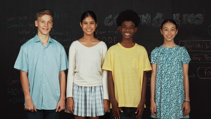 Group of smart multicultural teenager looking at camera at blackboard. Happy diverse children...