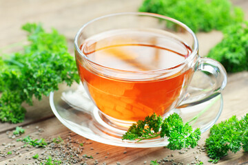 Parsley tea with fresh curly parsley leaves nearby on rustic wooden table, copy space, natural...