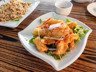 A serving of crispy deep fried squid, cuttlefish on a bed of lettuce, garnished with slices of onions and peppers.